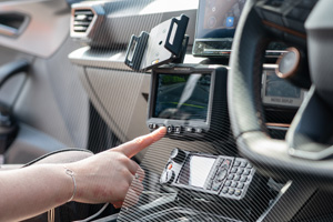 A police officer's hand adjusts the settings on a mounted Motorola Solutions M500 in-car video system display, located on the dashboard of a patrol vehicle. The screen shows a view from the camera. Other police radio equipment is visible below the display.
